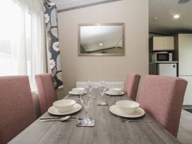 A dining table set with bowls glasses and cutlery with pink chairs near a window and kitchen area in Caravan 7 Plymouth