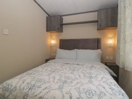 A bedroom with a bed with patterned bedding two wall lights and wooden cabinets above at Caravan 7 in Plymouth