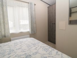 A bedroom with a bed near a window with floral curtains and a wardrobe in the corner at Caravan 7 in Plymouth
