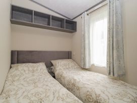 A bedroom with two single beds and patterned bedding under a window with floral curtains at Caravan 7 in Plymouth