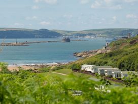 A coastal scene with caravans on green hills near a beach and a sea with a breakwater and lighthouse at Caravan 7 Plymouth