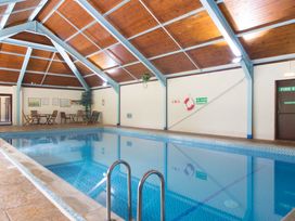 An indoor swimming pool with metal handrails wooden ceiling and tables with chairs at Caravan 7 in Plymouth