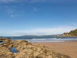 A sandy beach with rocky formations near the shore and the sea with hills and a lighthouse in the background at Caravan 7 in Plymouth