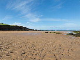 A sandy beach with rocks and a grassy cliff under a blue sky at Caravan 7 in Plymouth