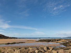 A sandy beach with rocks and seaweed near the water with ships in the distance at Caravan 7 in Plymouth