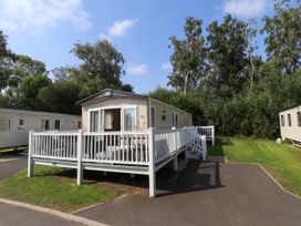 A static caravan with a white railing deck on a paved area surrounded by grass and trees at The Meadows 45 in Tattershall