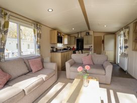 A living room with two sofas and a wooden coffee table with flowers next to a kitchen at The Meadows 45 in Tattershall