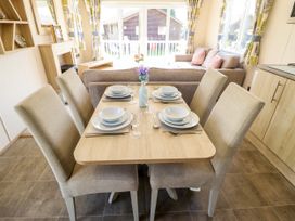 A dining table set for four with chairs in a living area with sofas and large windows at The Meadows 45 in Tattershall