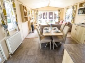 A dining area with a table set for six chairs next to a living room with a sofa and windows with patterned curtains at The Meadows 45 in Tattershall