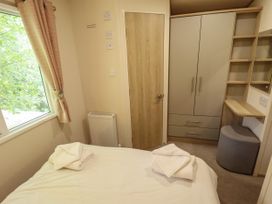 A bedroom with a bed, a window with curtains, a radiator, a wooden door, a wardrobe, shelving, and a stool at The Meadows 45 in Tattershall