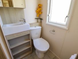 A small bathroom with a sink, toilet, yellow flowers on the shelf, and a window at The Meadows 45 in Tattershall