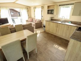 An open kitchen and dining area with a wooden table and chairs adjacent to a living room with sofas and a television at The Meadows 45 in Tattershall