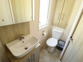 A small bathroom with a sink and mirror a toilet a trash bin and wooden cabinets at The Meadows 45 in Tattershall