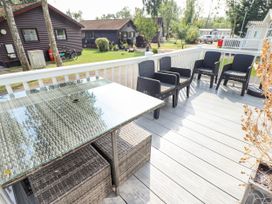 An outdoor deck with a glass table and four black chairs with cushions at The Meadows 45 in Tattershall