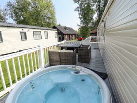 An outdoor deck with a hot tub a table with four chairs and nearby caravans and trees at The Meadows 45 in Tattershall
