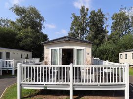 A beige mobile home with white railing and outdoor furniture surrounded by trees at The Meadows 45 in Tattershall