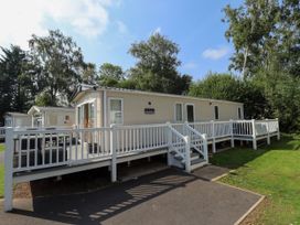 A beige mobile home with a white railing deck and stairs surrounded by trees and grass at The Meadows 45 in Tattershall