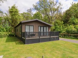 A brown cabin with a grey deck railing on a grassy plot surrounded by trees at 18 Manleigh Park in Combe Martin