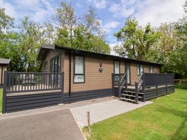 A single story wooden cabin with a deck and stairs surrounded by grass and trees at 18 Manleigh Park in Combe Martin