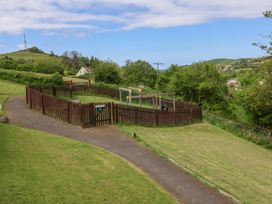 A fenced playground with swings and a slide along a paved path in a grassy area at 18 Manleigh Park in Combe Martin