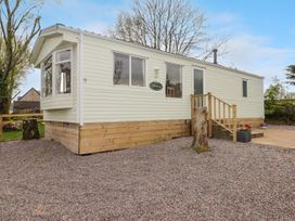 A white mobile home with wooden skirting and small stairs on a gravel lot with trees in the background at Grandads Shack in Trevethin near Pontynewynydd