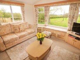 A sitting area with a sofa, coffee table with flowers, TV, window seats, and large windows showing a green lawn at Grandads Shack in Trevethin near Pontynewynydd