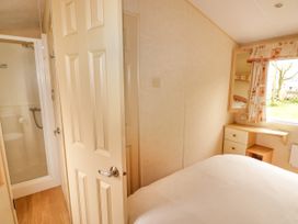 A bedroom with a bed a window with curtains a small desk and a door leading to a bathroom at Grandads Shack in Trevethin near Pontynewynydd