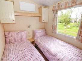 A bedroom with two single beds covered with pink polka dot bedding next to a window showing a green outdoor space at Grandads Shack in Trevethin near Pontynewynydd