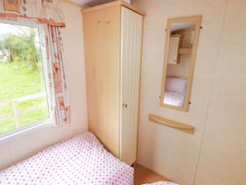 A bedroom with two beds with polka dot bedding a wooden wardrobe a wall mirror and a window with curtains at Grandads Shack Trevethin near Pontynewynydd