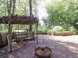 A garden with a table and chairs under a wooden shelter at Tanglewood Shepherds Hut in Welshpool