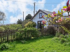 A garden with grass and flowering plants in front of a small house with a wooden fence and a partly cloudy sky at Dolphin Bach in Dolphin