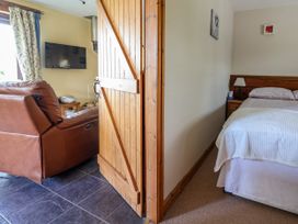 A view of a living room with a brown leather sofa television and radio and a partially open wooden door leading to a bedroom with a bed and bedside table at Dolphin Bach in Dolphin