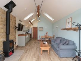 An open plan living room and kitchen with a wood burning stove wooden dining table sofa and wall-mounted tv at The Cart Shed Barwick near Yeovil Somerset