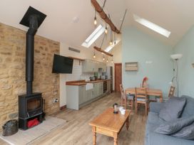 A kitchen area with wooden countertops and a dining table with chairs next to a living space with a couch and a wood burning stove at The Cart Shed in Barwick near Yeovil Somerset