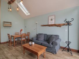 A living room with a wooden dining table with four chairs a blue sofa with cushions a wooden coffee table a coat rack and a skylight window at The Cart Shed in Barwick near Yeovil Somerset