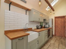 A kitchen with wooden countertops, green cabinets, a white farmhouse sink, toaster, microwave, and wooden door at The Cart Shed in Barwick near Yeovil Somerset