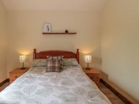 A bedroom with a double bed with leaf patterned bedding two bedside tables with lamps and a shelf with a picture and pinecone at The Cart Shed in Barwick near Yeovil Somerset