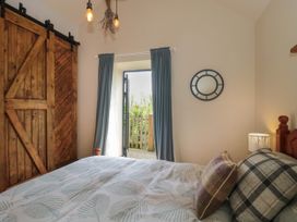 A bedroom with a wooden sliding door bed with pillows and a lamp next to a door with curtains at The Cart Shed in Barwick near Yeovil Somerset