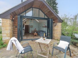 An outdoor patio with two chairs and a small table with a bottle and glasses in front of an open living space at The Cart Shed in Barwick near Yeovil Somerset