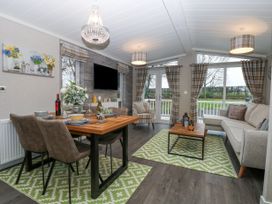 A combined dining and living room with a wooden dining table set with dishes and wine bottles and a seating area with a sofa and armchair at Wurzburc in Swaffham