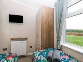 A bedroom with two beds featuring floral covers a wardrobe a wall-mounted television and a window with curtains at Wurzburc in Swaffham