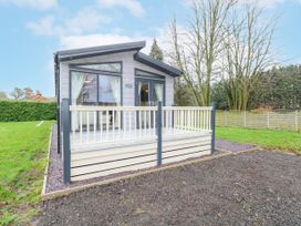 A small modern cabin with glass doors and windows and a wooden deck surrounded by grass and trees at Wurzburc in Swaffham