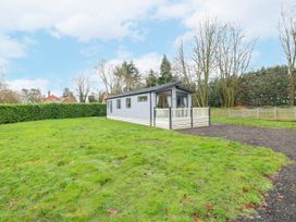 A small rectangular house with a porch and multiple windows on a grassy plot with trees and fences at Wurzburc in Swaffham
