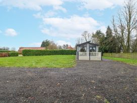 A small house with a porch and large windows surrounded by grass and trees at Wurzburc in Swaffham