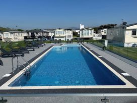 An outdoor swimming pool with lounge chairs and tables surrounded by mobile homes at Cornerstone Near Caernarfon