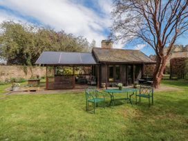 A garden with a small cabin a green metal table and two chairs on the grass at Snape Castle Garden Lodge in Snape near Bedale