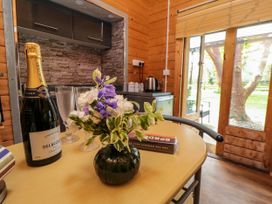 A wooden dining table with a bottle of champagne flowers and glasses in a kitchen with glass doors showing a garden at Snape Castle Garden Lodge in Snape near Bedale