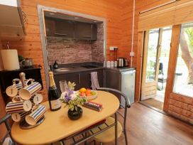 A kitchen with a table holding mugs a bottle a bowl of fruit and flowers at Snape Castle Garden Lodge in Snape near Bedale