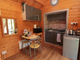 A small kitchen area with wooden walls a table with two chairs a microwave fridge kettle and toaster at Snape Castle Garden Lodge in Snape near Bedale