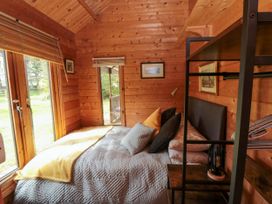 A wooden bedroom with a bed pillows blankets a metal shelf and a glass door at Snape Castle Garden Lodge Snape near Bedale